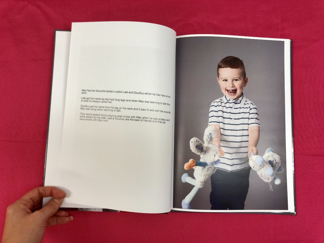 An opened book, with text on the left hand page and a picture of a young boy, in a striped t shirt, holding two cuddly toys on the right page.