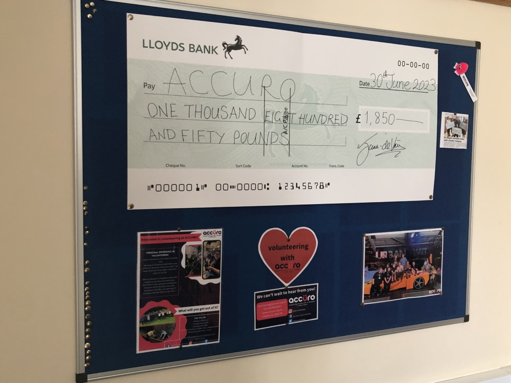 Dark blue display board with a large donation cheque and four colourful Accuro posters.