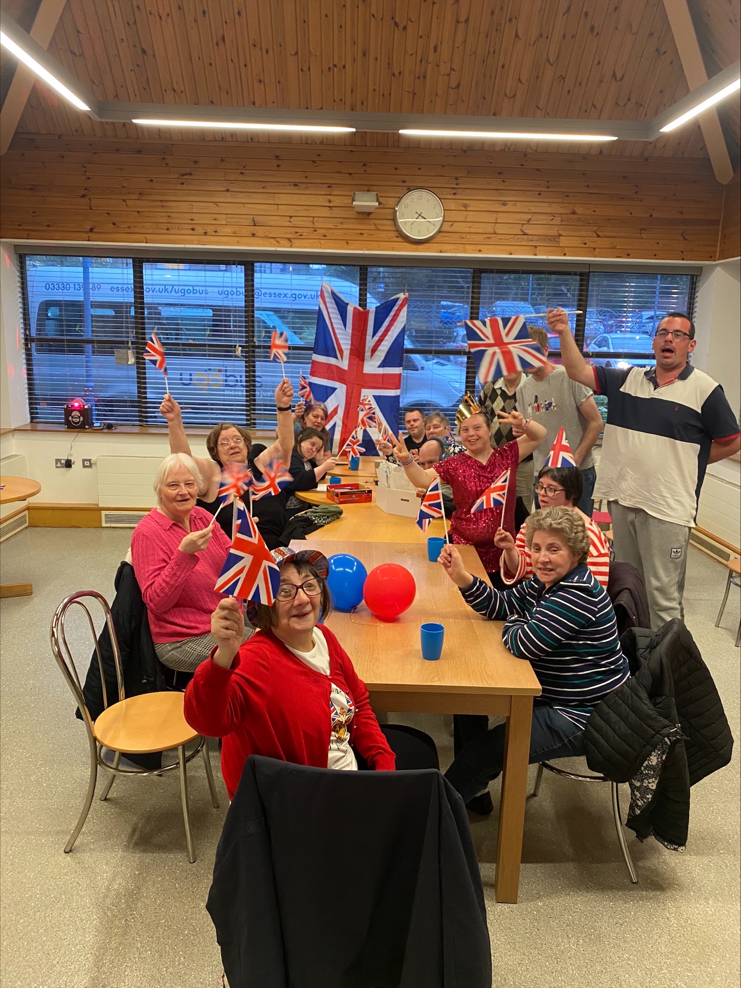 Adult Friendship Scheme members celebrating the King's Coronation with a party. Members are holding the British flag.